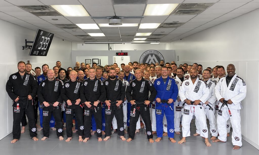 317 Jiu-Jitsu instructors and members in gis lined up on the mats at the academy